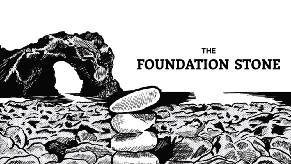 Title panel for "The Foundation Stone". Stacked stones in the foreground on a rocky beach. A large rock archway is visible in the background. 
